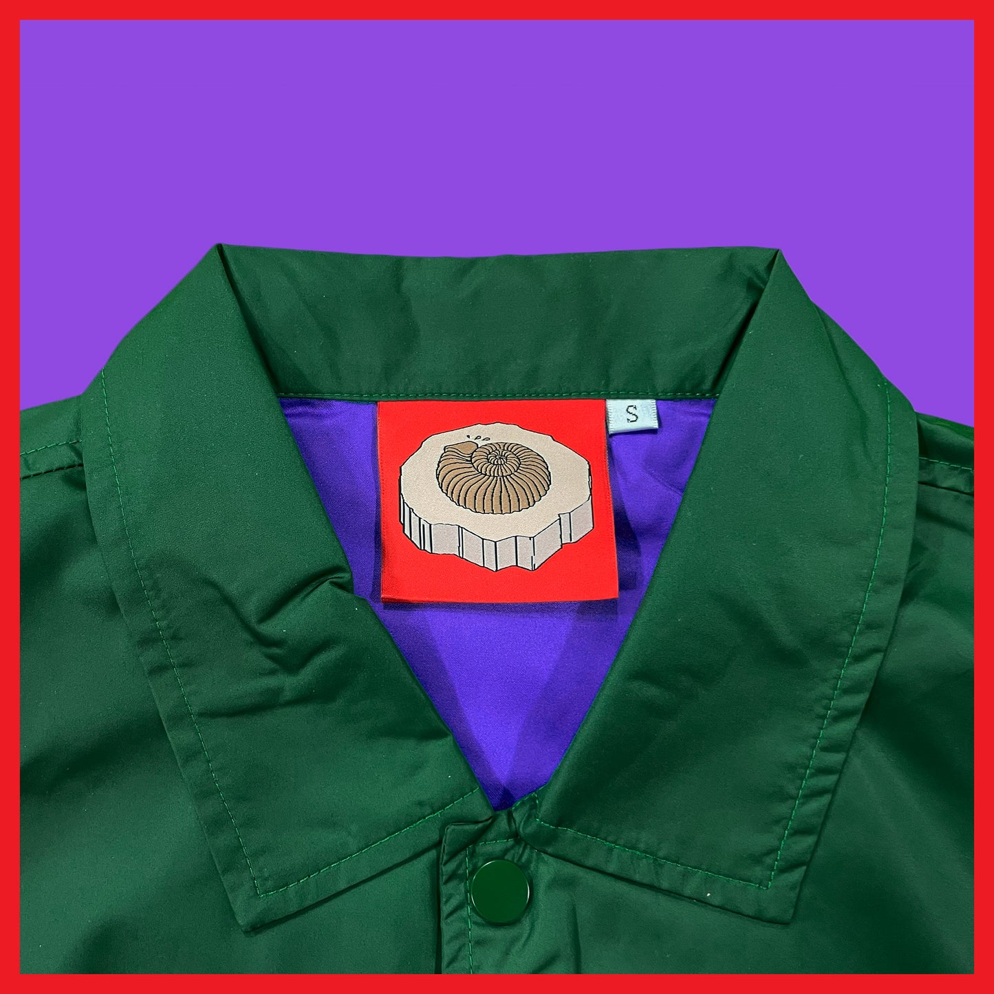 Close-up of Pupik The Fossil Hunter Windbreaker collar with red fossil logo tag in green color
