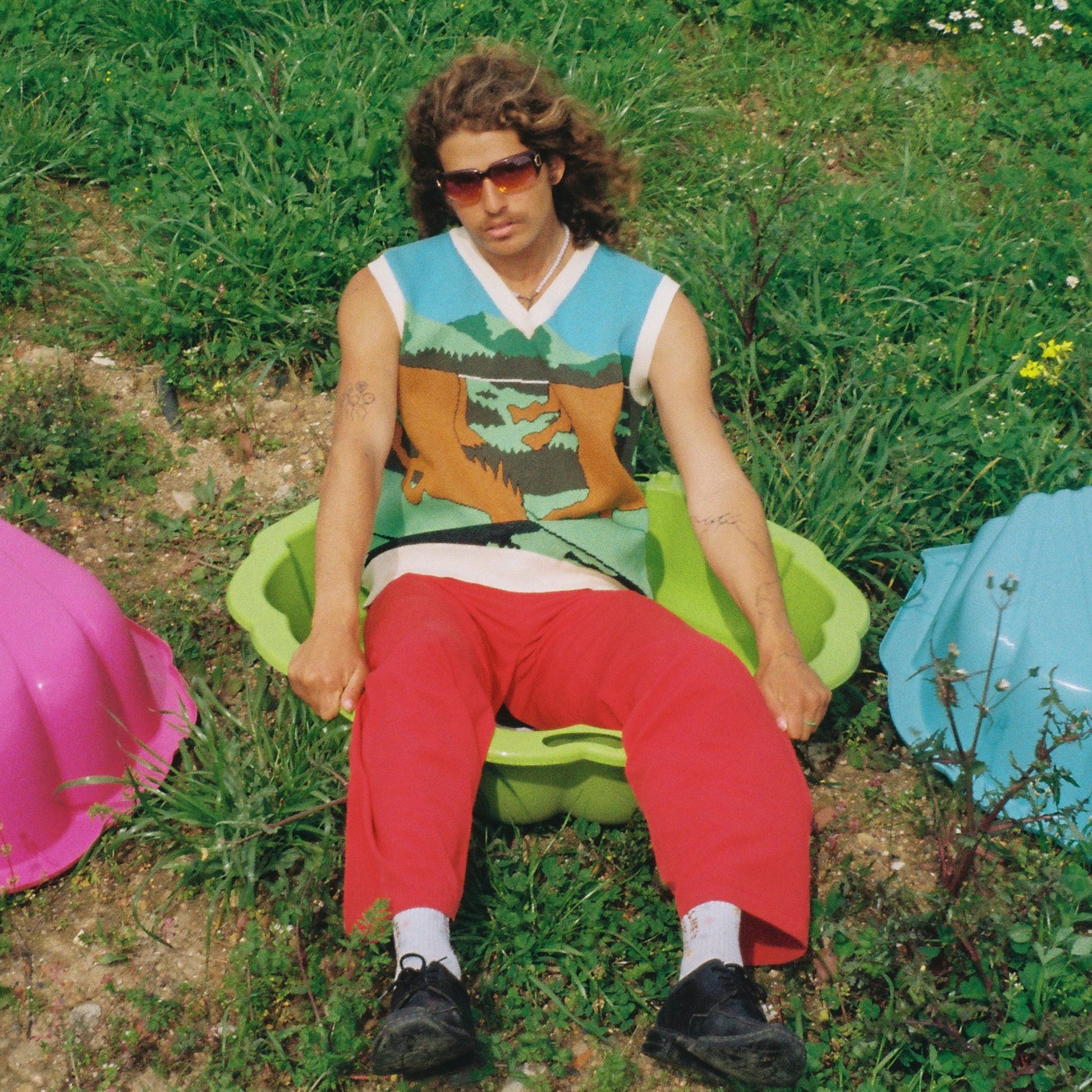 Person sitting on a colorful chair in a grassy area with other chairs around