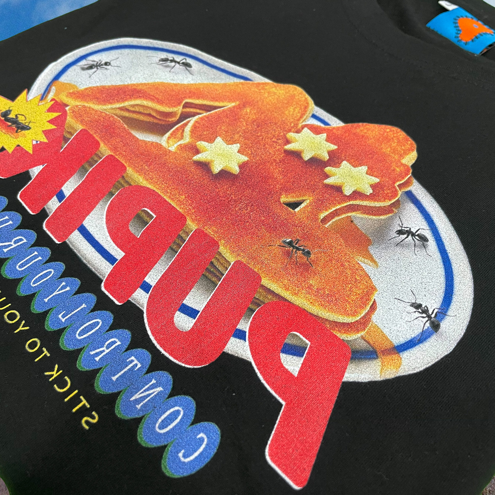 Close-up of the Pupik Stick To Your Values shirt print showing a surreal pancake-shaped female silhouette with star censors, crawling ants, and bold red Pupik logo with the phrase ‘Control Your Urges – Stick to Your Values
