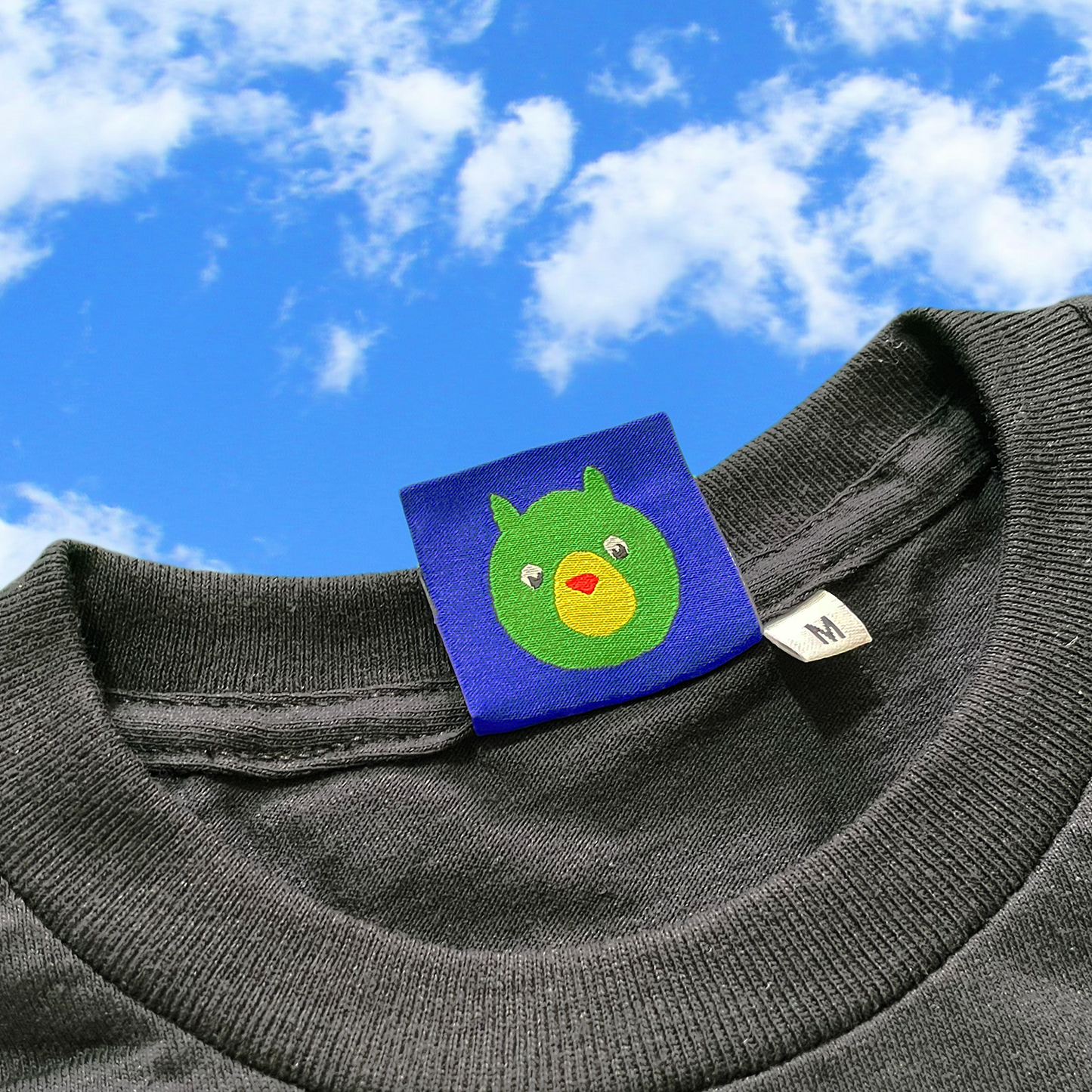 black shirt with a colorful label featuring a cartoon face against a blue sky.