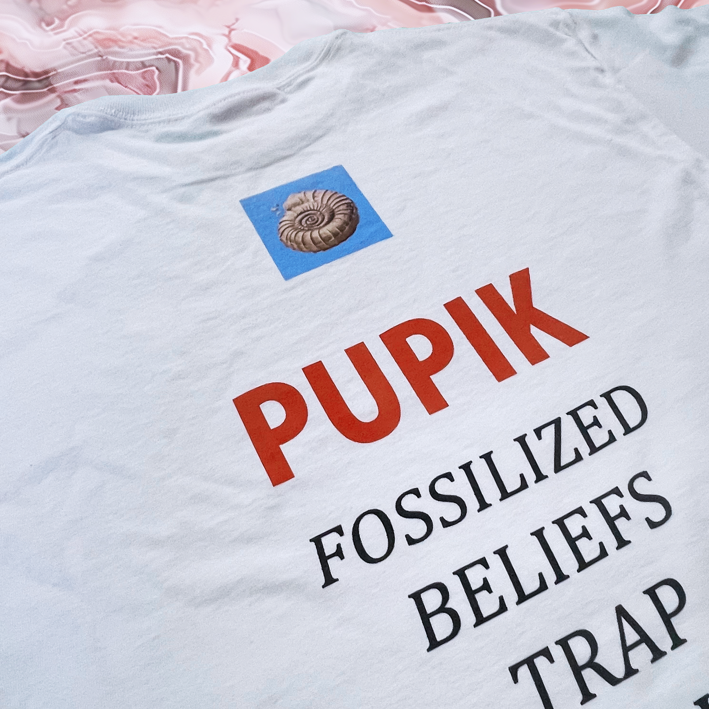 White t-shirt with red and black text and a blue square logo on a pink floral background