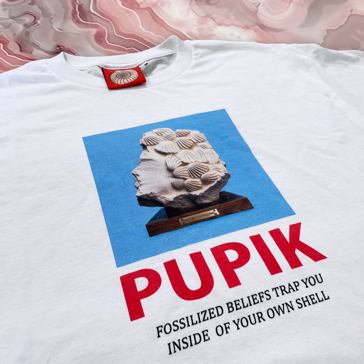 White t-shirt with a graphic of a fossilized rock and text on a pink and white marbled background