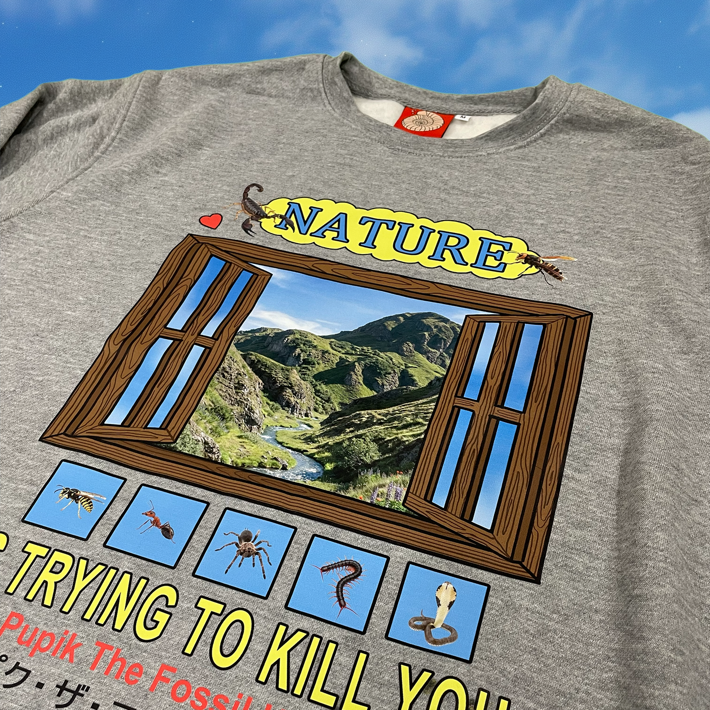 Gray t-shirt with a graphic design of a window looking out at nature and text on a blue sky background