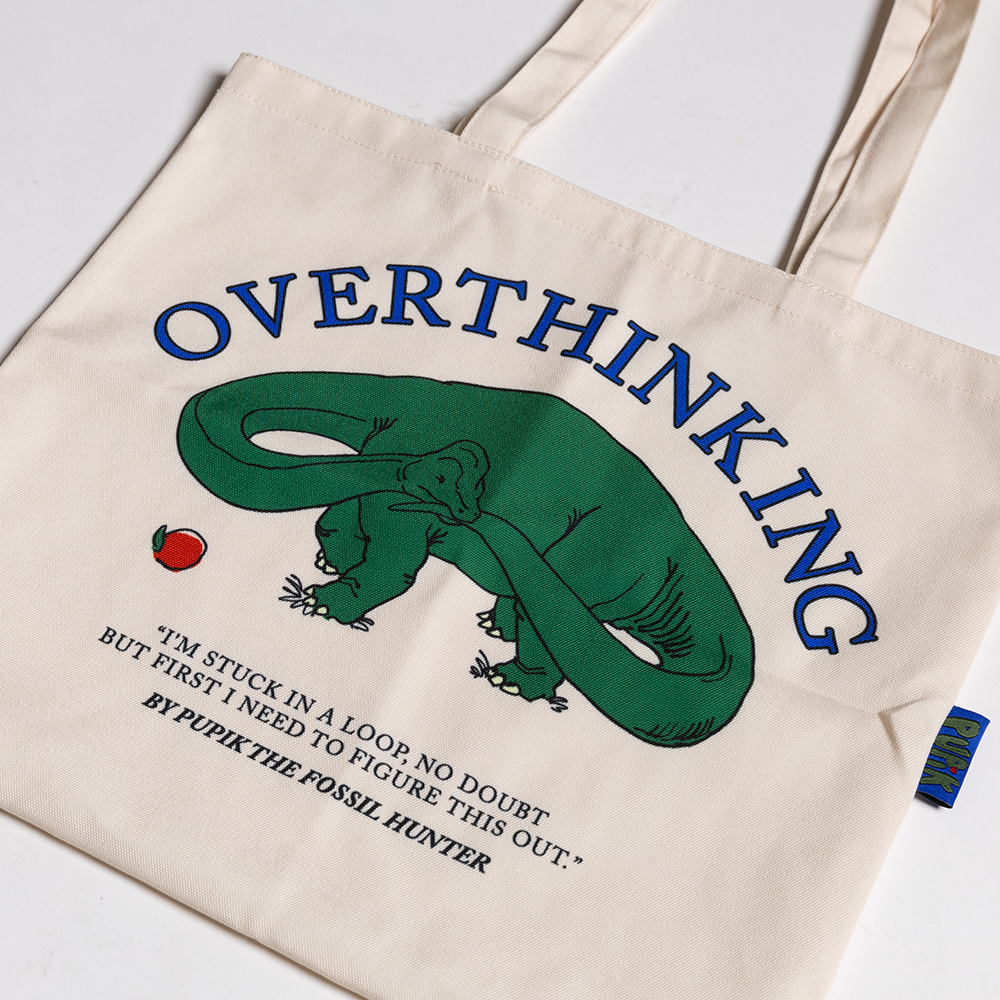 Beige tote bag with a green dinosaur illustration and text on a white background