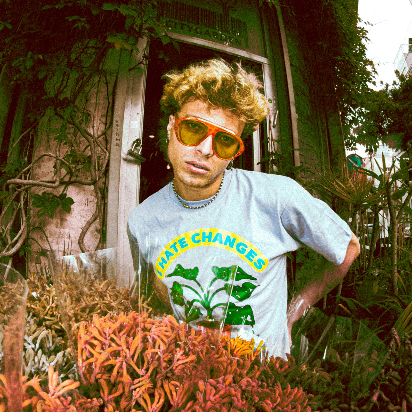 Person wearing a 'hATE CHANGES' t-shirt with sunglasses in front of a building with plants.